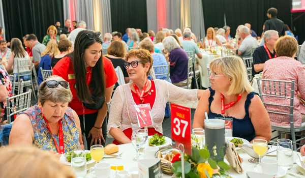Alumni interacting and enjoying lunch at an the President's Milestone Lunch event, with attendees seated at a table, name tags visible.