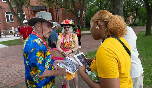Alumni enjoying a guided campus tour, with one guide showing photos to a group of attendees outside a historic building on campus.